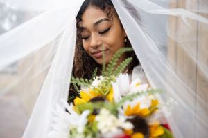 A close-up of a bride with colorful bouquet peeking through her white veil.