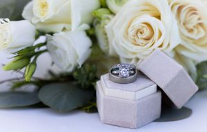 Diamond engagement ring in grey hexagonal box surrounded by white roses.