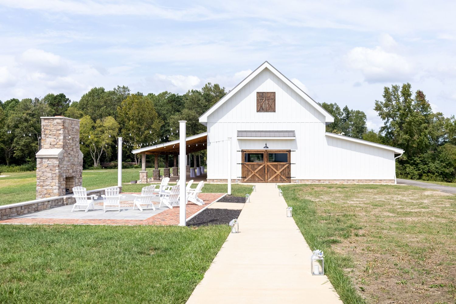 A white modern barn wedding venue with stone chimney and concrete walkway.