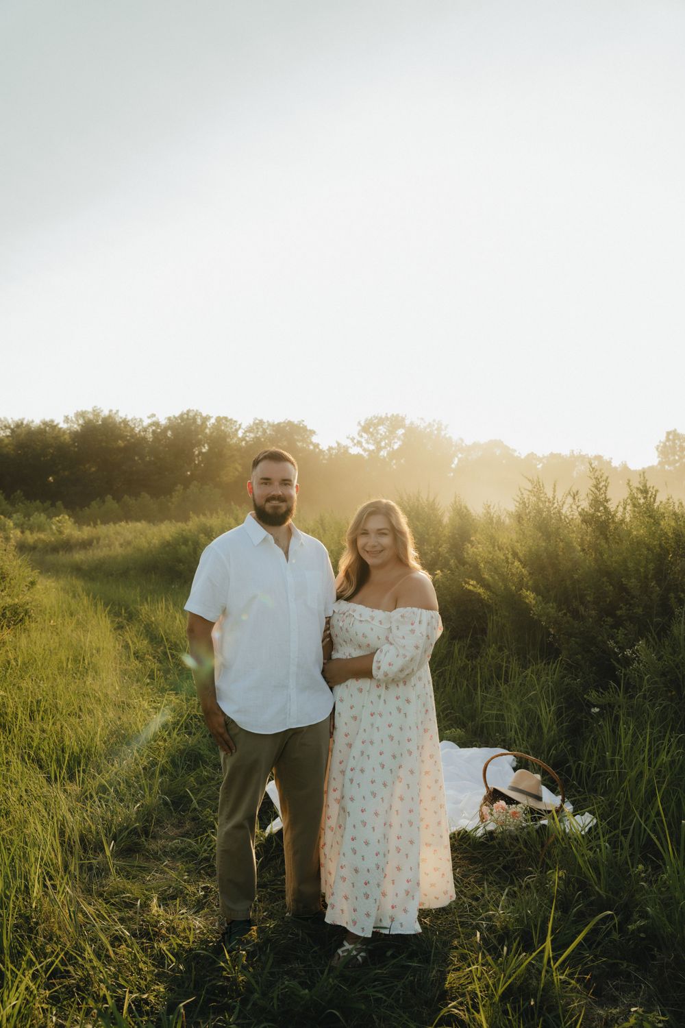 Couple standing together near a beautifully arranged picnic setup, bathed in warm, golden sunlight.