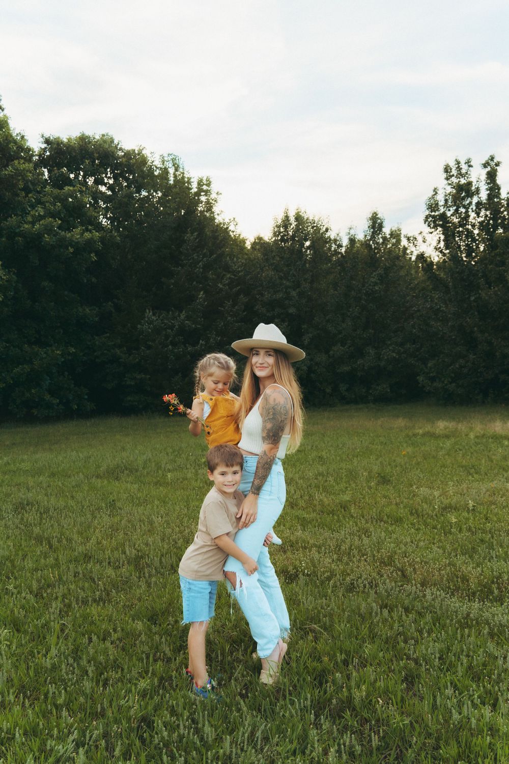 Mom posing with her son and daughter in front of a lush wooded backdrop, all smiling and standing close together.