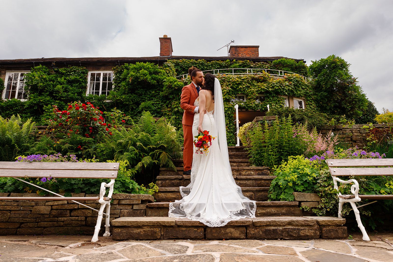 Bride and groom share a romantic kiss on stone steps of an ivy-covered country house wedding venue.