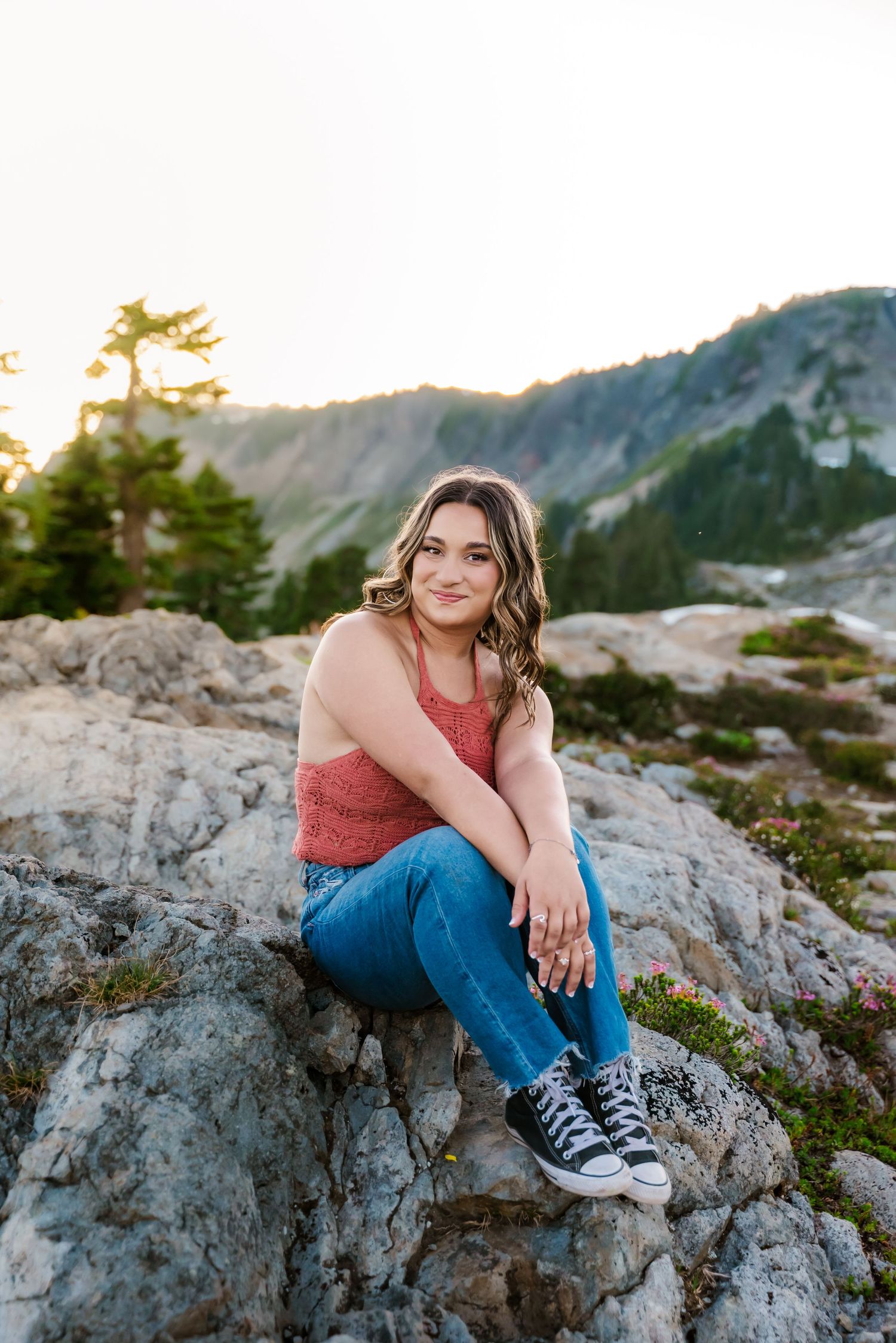 senior girl smiles, sitting on rocks at artist's point backed by sunset glow