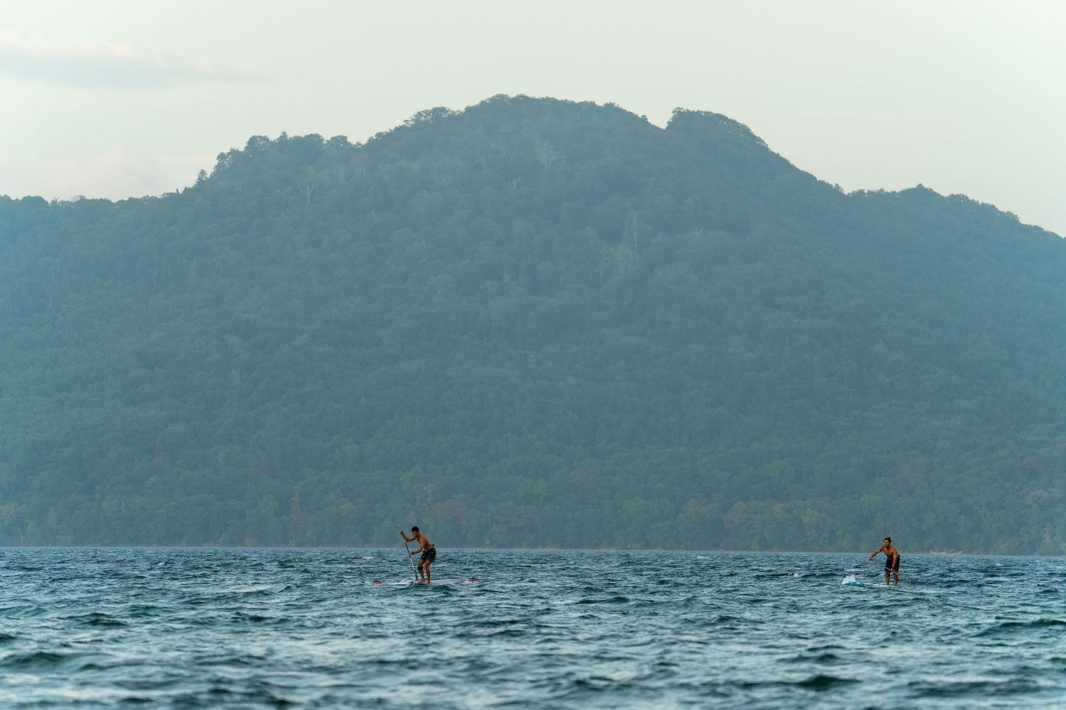 Scenic mountain lake view with distant paddleboarders on calm waters.