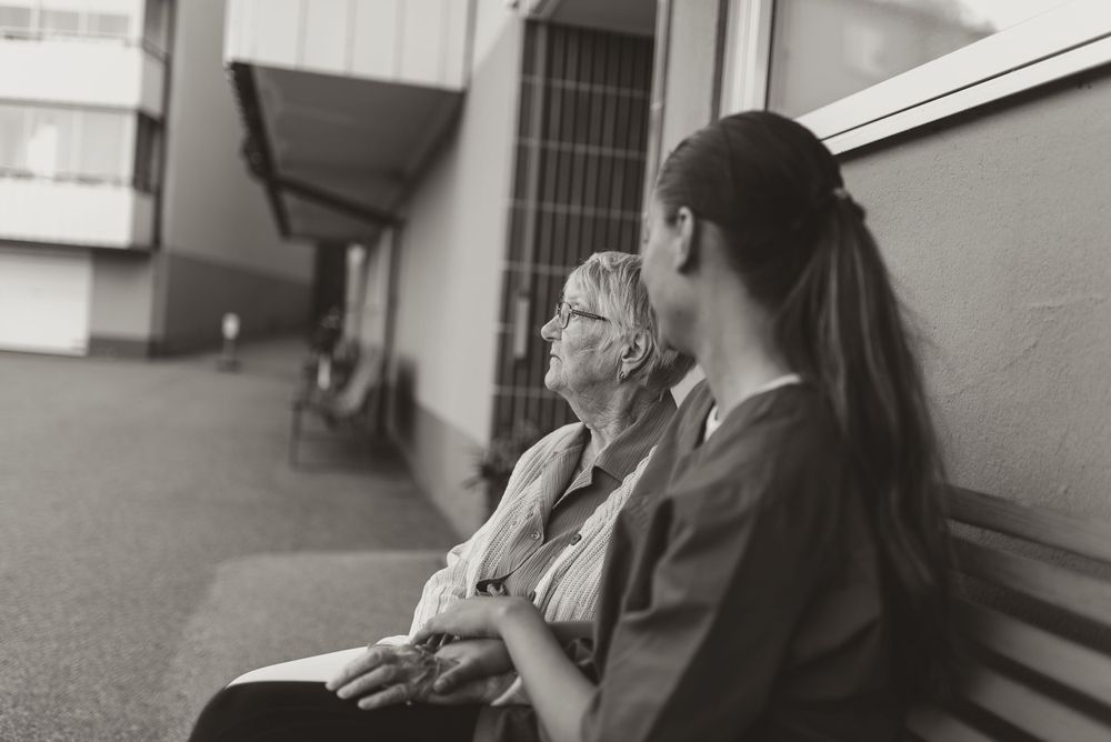 A black and white image showing two people sitting together on an outdoor bench.