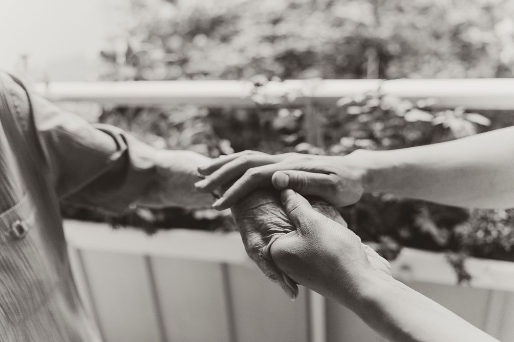 A black and white close-up photo of hands gently touching on an outdoor balcony.