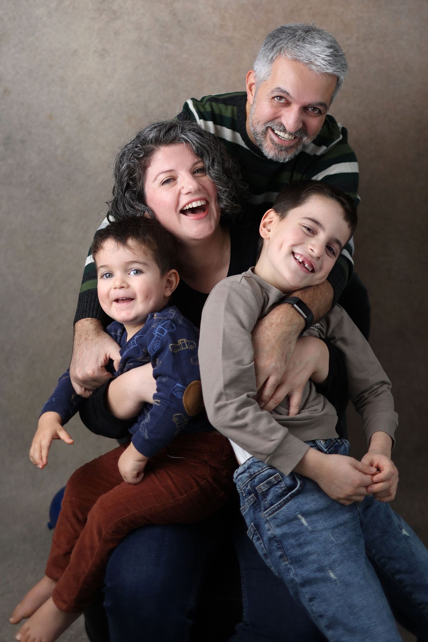 Family portrait showing joyful laughter and playful poses against a neutral background.