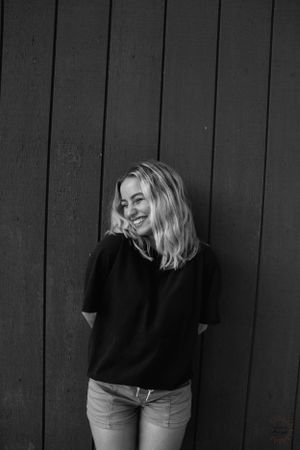 Photo of girl leaning against wall, smiling, looking away from camera, in black and white.