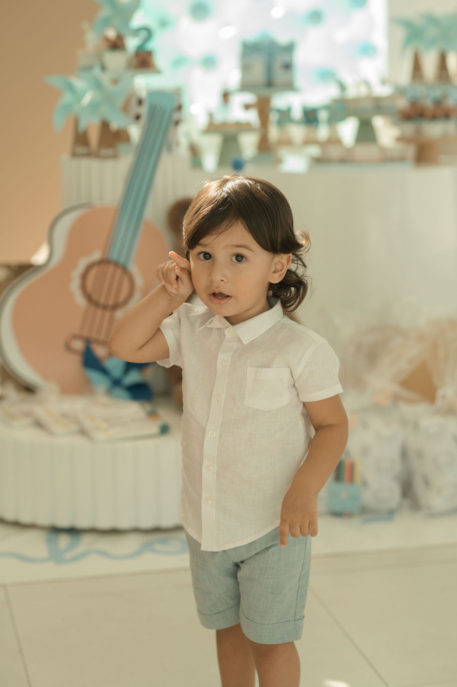 Young child in white shirt and shorts standing in front of decorative guitar wall display.