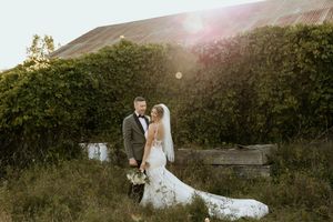 A couple stands together in a garden during sunset while lens flares create a dreamy atmosphere in their wedding photos.