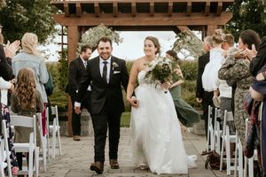 Wedding ceremony setup outdoors with white chairs and wooden pergola against a scenic natural backdrop at sunset.