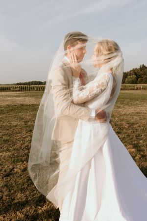 Romantic sequence of bride and groom embracing with flowing white veil in sunlit field at golden hour.