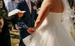 Close-up of couple holding hands during outdoor wedding ceremony with officiant in background.