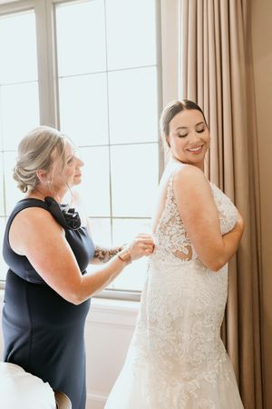 A special moment of helping with wedding dress preparations by a large window with natural light streaming in.
