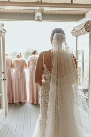 Wedding dresses and pink bridesmaid gowns hanging on display in a bright, sunlit bridal suite.