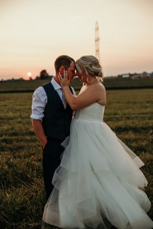 Romantic sunset portrait of newlyweds embracing in rural field with evening sky.