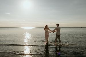 Three people enjoy a tranquil sunset swim in a serene lake with sun reflections on the rippling water.