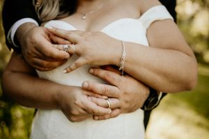 Close-up of hands exchanging wedding rings during an outdoor ceremony.