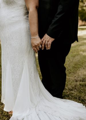 Close-up of bride and groom holding hands showing wedding dress train.