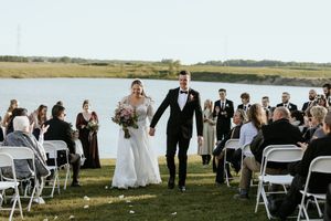 Row of white chairs set up for an outdoor wedding ceremony with guests seated against a scenic countryside backdrop.