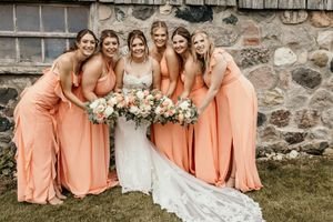 Bridesmaids in matching peach dresses gather around bride in white for group photo.