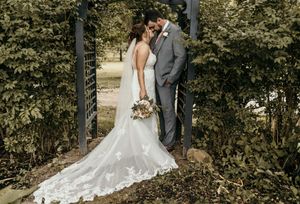 Romantic wedding portrait of couple under garden archway with white lace dress trailing behind.