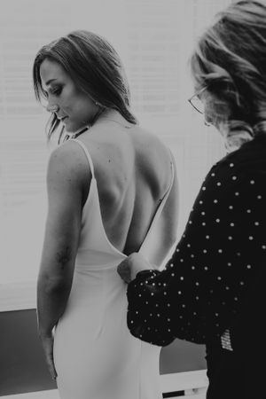 Back view of a bride in a sleek white dress during final fitting preparations.