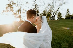 Wedding couple embraces in golden sunlight as bride's white veil flows dramatically in the breeze.