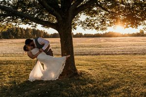 Sunset wedding photo of couple embracing under large tree in open field.