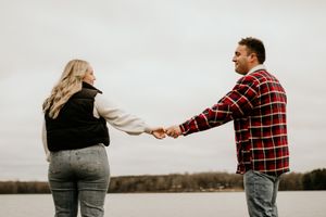 Couple holding hands while standing by a lake in casual winter clothing.