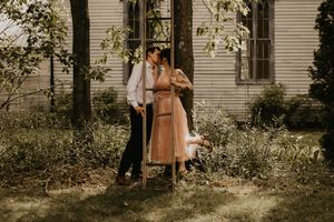 A romantic outdoor portrait against a white house with a couple in vintage-inspired clothing.