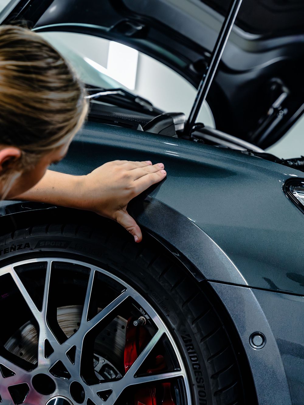 Professional applying ceramic coating protection to a luxury car's black wheel and tire during automotive detailing service.