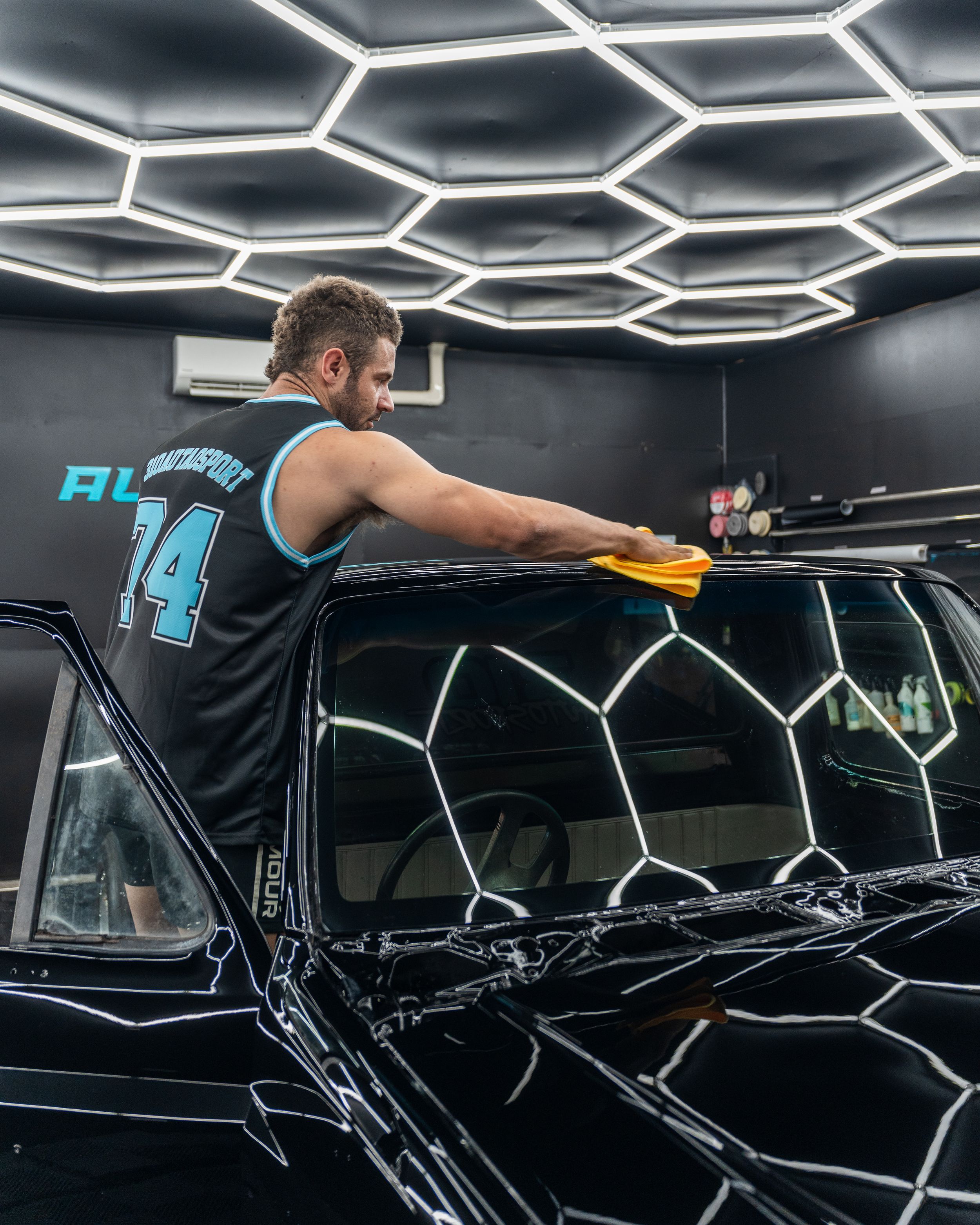 Professional car detailing session in modern facility with hexagonal ceiling lights.