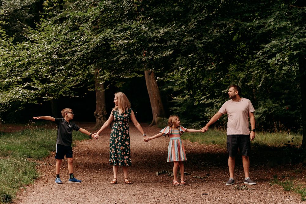 A family walking hand in hand in a scenic forest path surrounded by lush green trees and dappled sunlight.