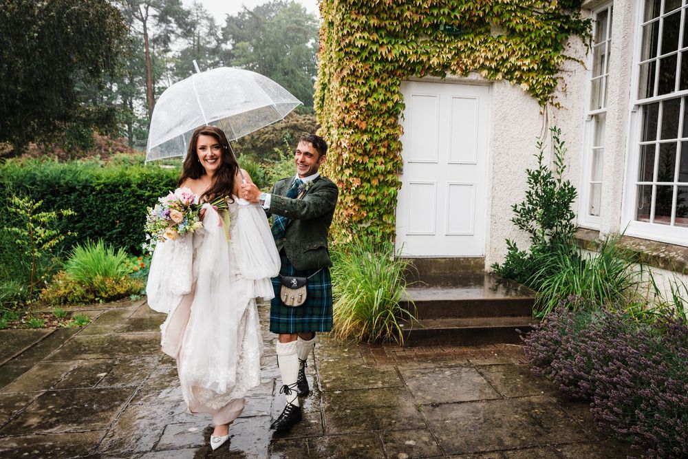 Rainy wedding with bride and groom walking across the gardens at Rufflets Hotel, St Andrews and holding an umbrella