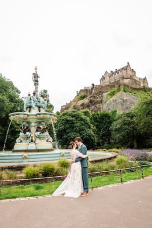 Wedding photo at Princes street gardens with Edinburgh Castle as backdrop.  Bride and groom hugging