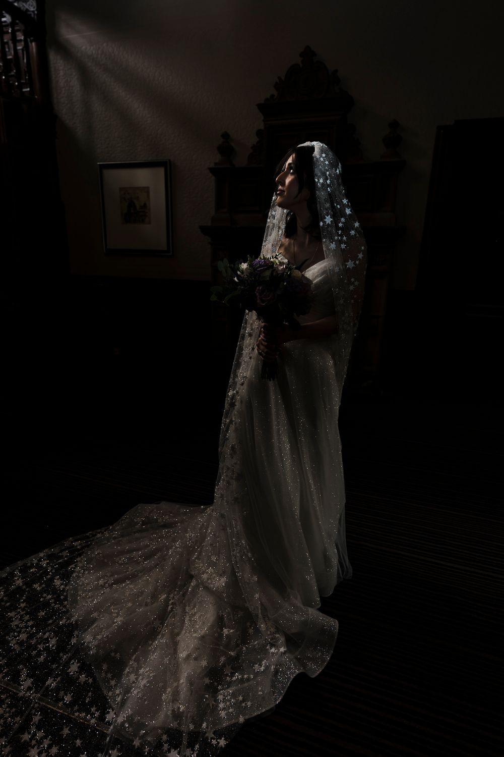 Bride with long cathedral veil standing in slit of light in Dundee at Taypark House