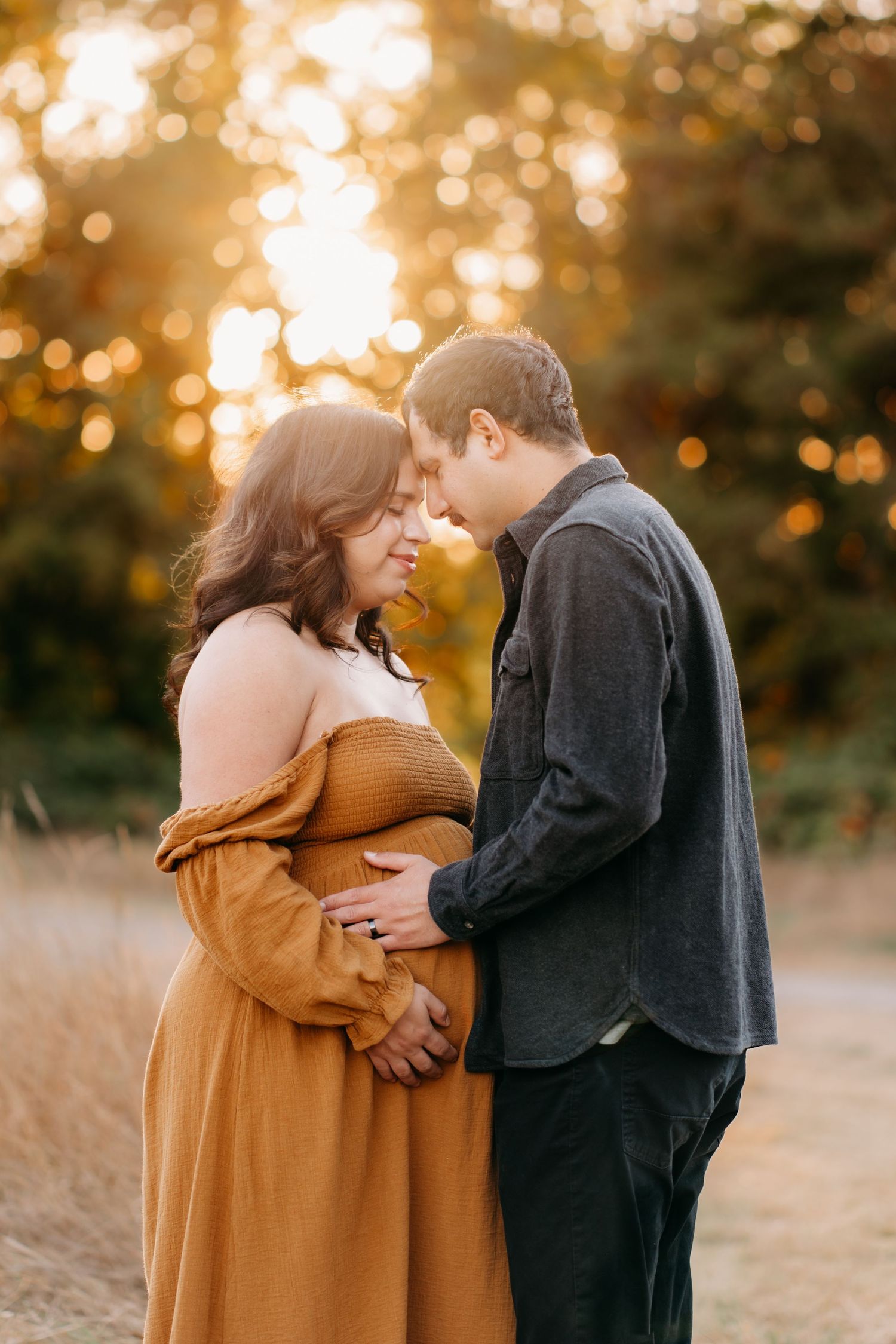A couple shares an intimate moment in a golden autumn field during sunset during maternity photos in Tacoma.