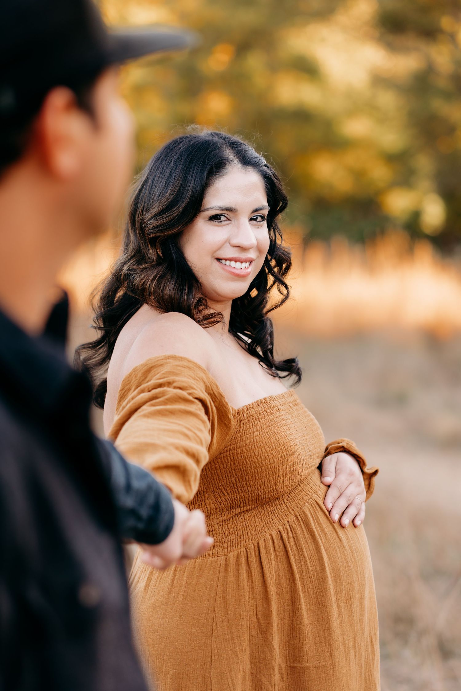 A series of four maternity photos showing a woman in a brown sweater outdoors during golden hour.
