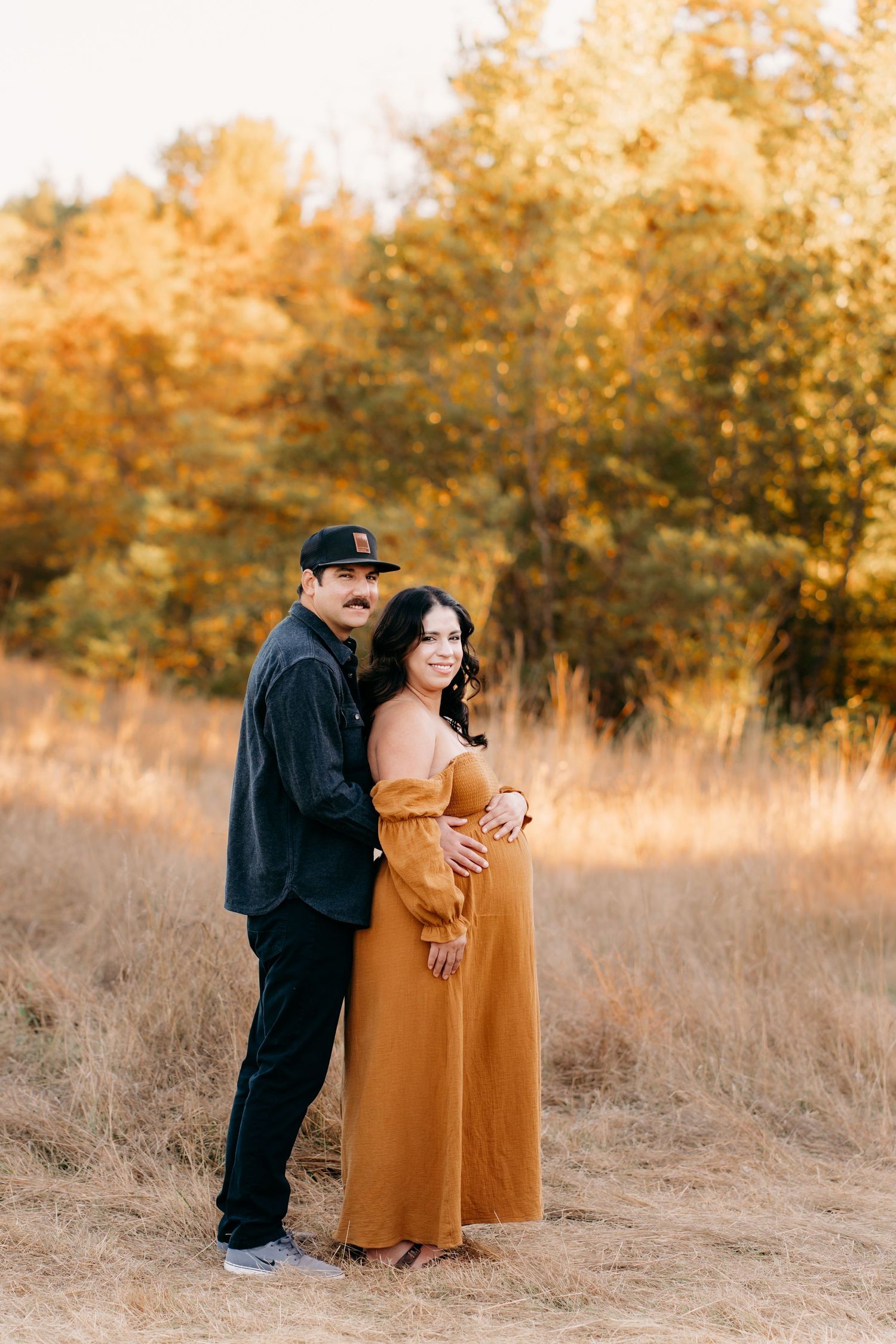 A couple shares an intimate moment in a golden autumn field during sunset during maternity photos in Tacoma.