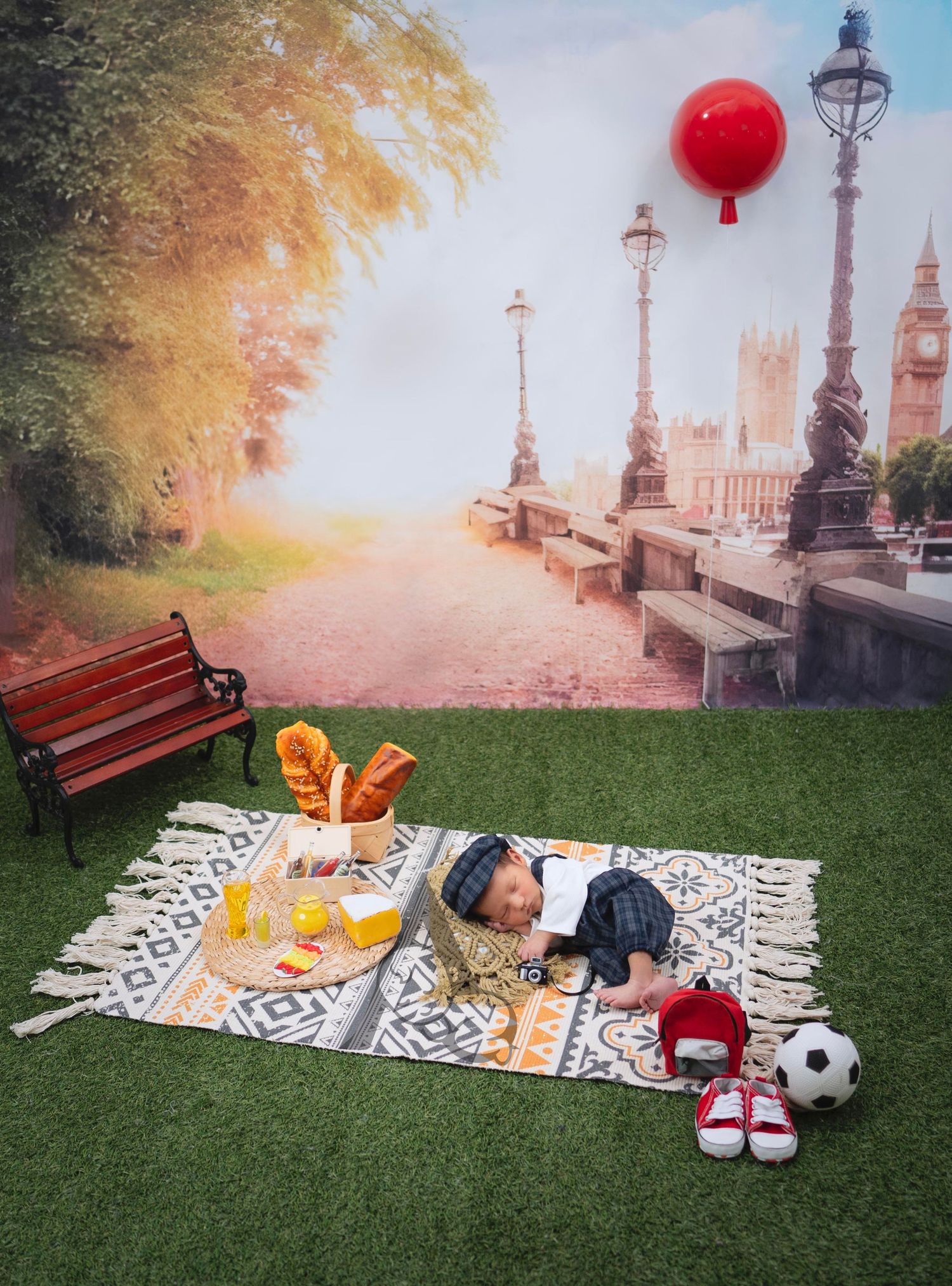 Picnic setup in park with blanket, food, and soccer ball near ornate lampposts.