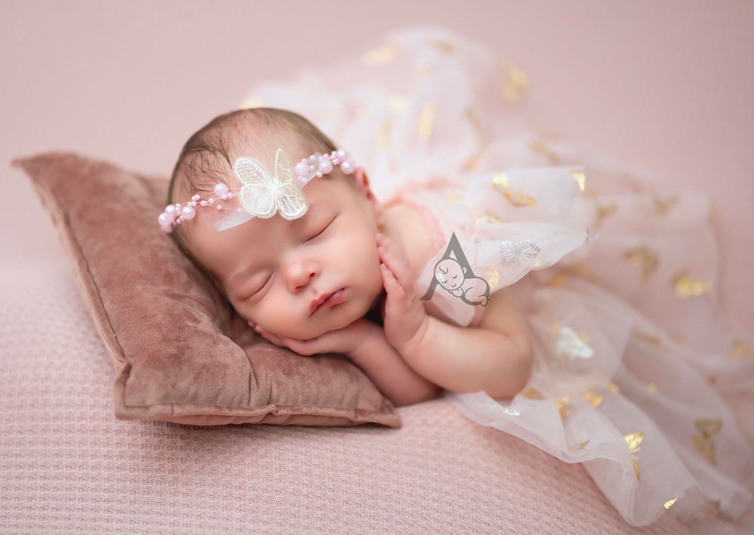 Sleeping newborn wearing delicate floral headband and tulle dress rests peacefully on brown pillow against pink backdrop.