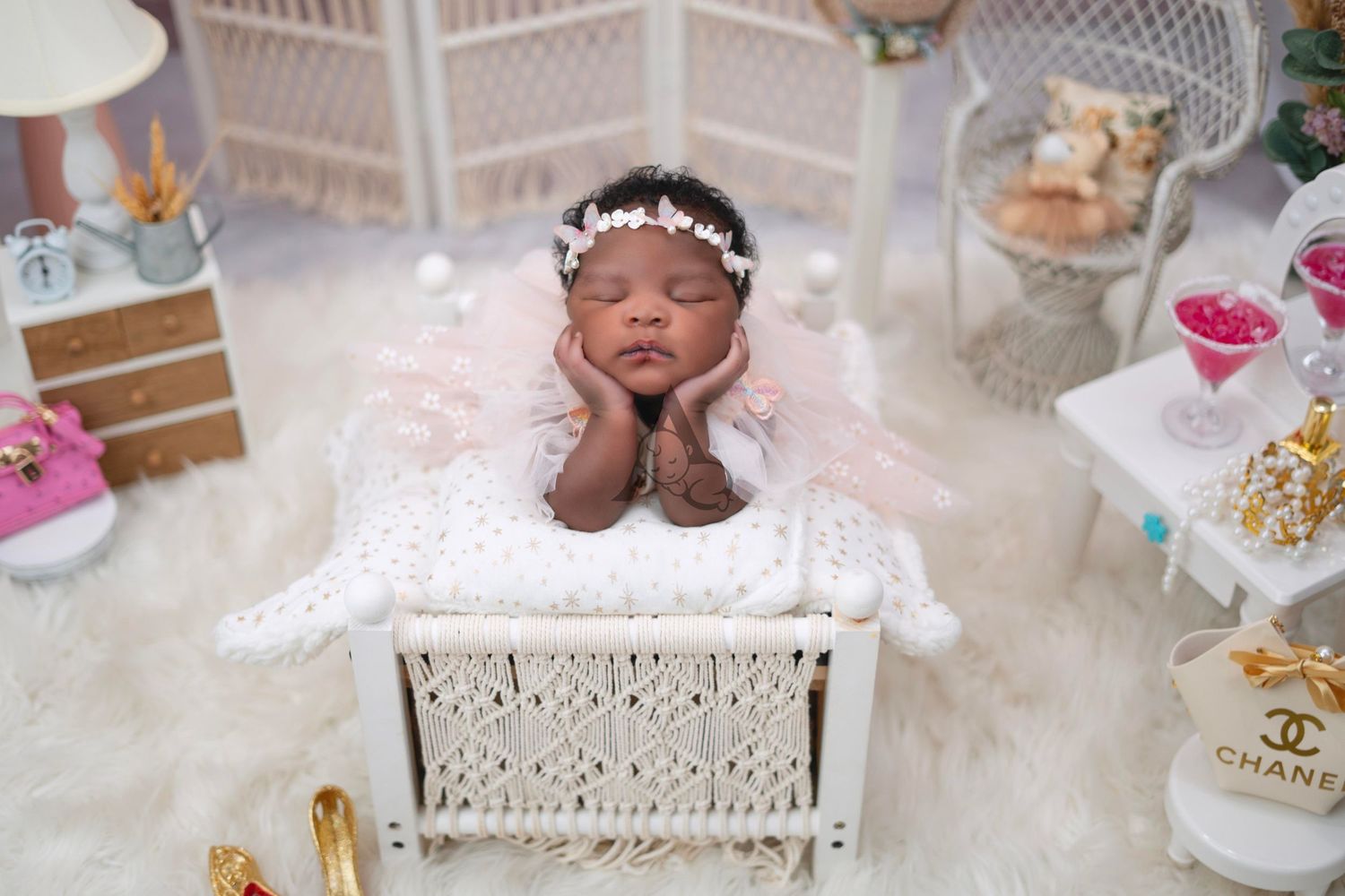 Newborn baby resting on white wicker chair with delicate accessories and soft pink decor.