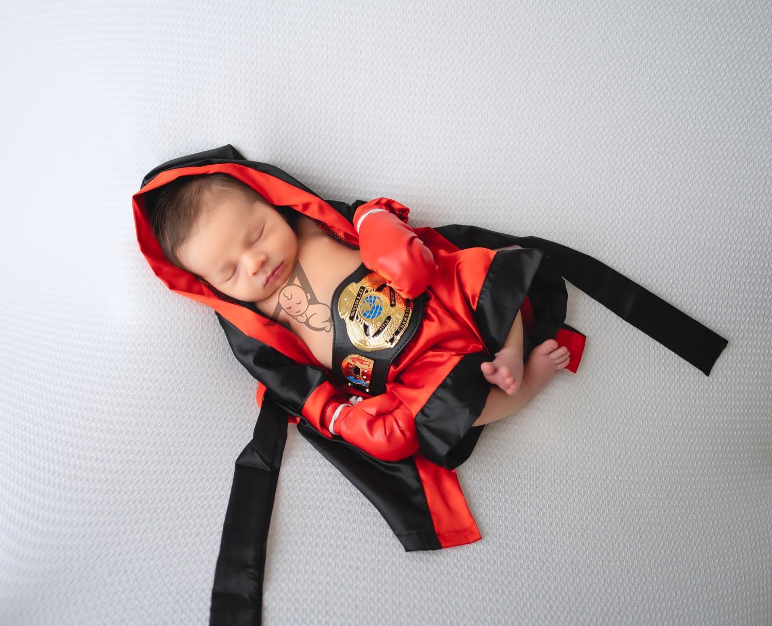 Baby sleeping peacefully in red and black hooded outfit on white background.