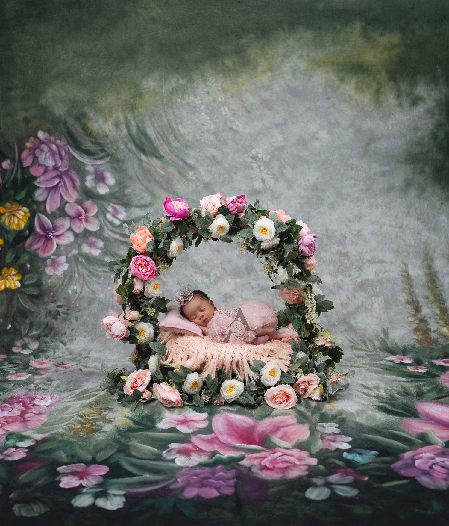 Sleeping baby in floral wreath surrounded by pink roses against moody painted backdrop.