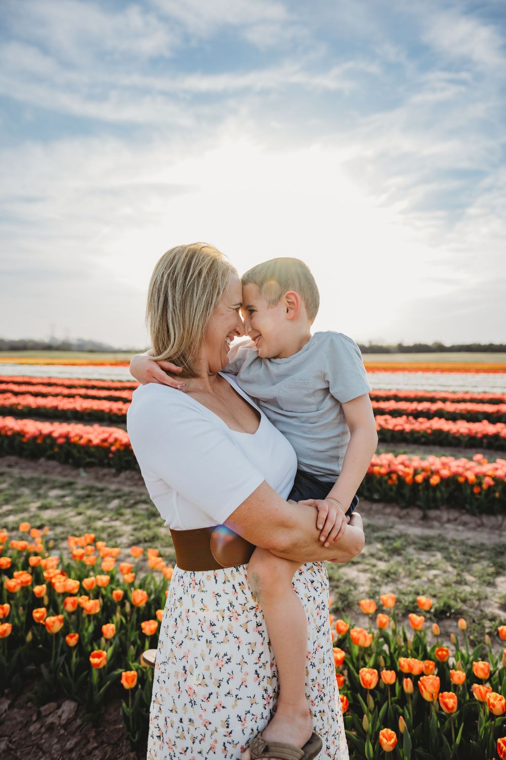 A joyful moment shared between a parent and child in a vibrant orange tulip field under a bright cloudy sky.
