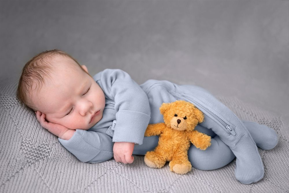 newborn photography studio ashford kent photo of a baby in blue laying onside with teddy infront  timeless photography creating memories