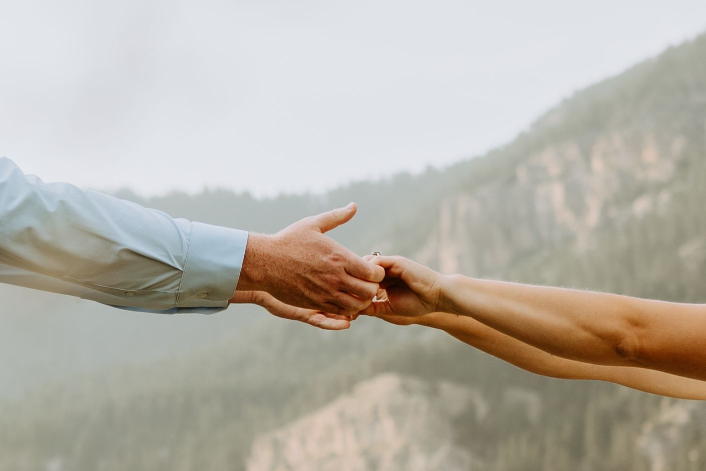 Close-up of two hands reaching out to connect against a dramatic mountain backdrop.