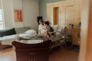 Nurse assisting new mother in hospital room bed during postpartum recovery after childbirth.
