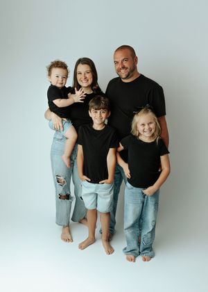 Family of five in matching black shirts and jeans posing together in professional studio portrait.
